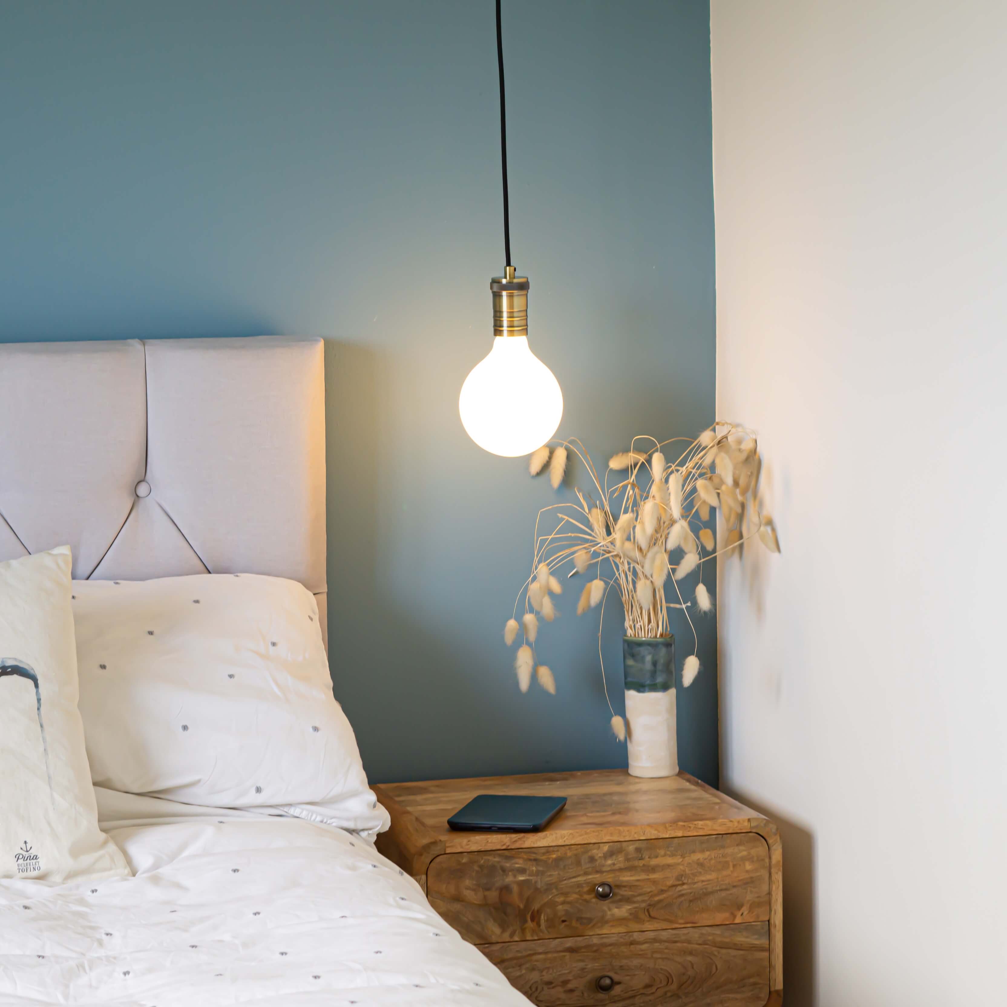 antique bronze pendant light and straight cable with luna bulb hanging above the bedside table