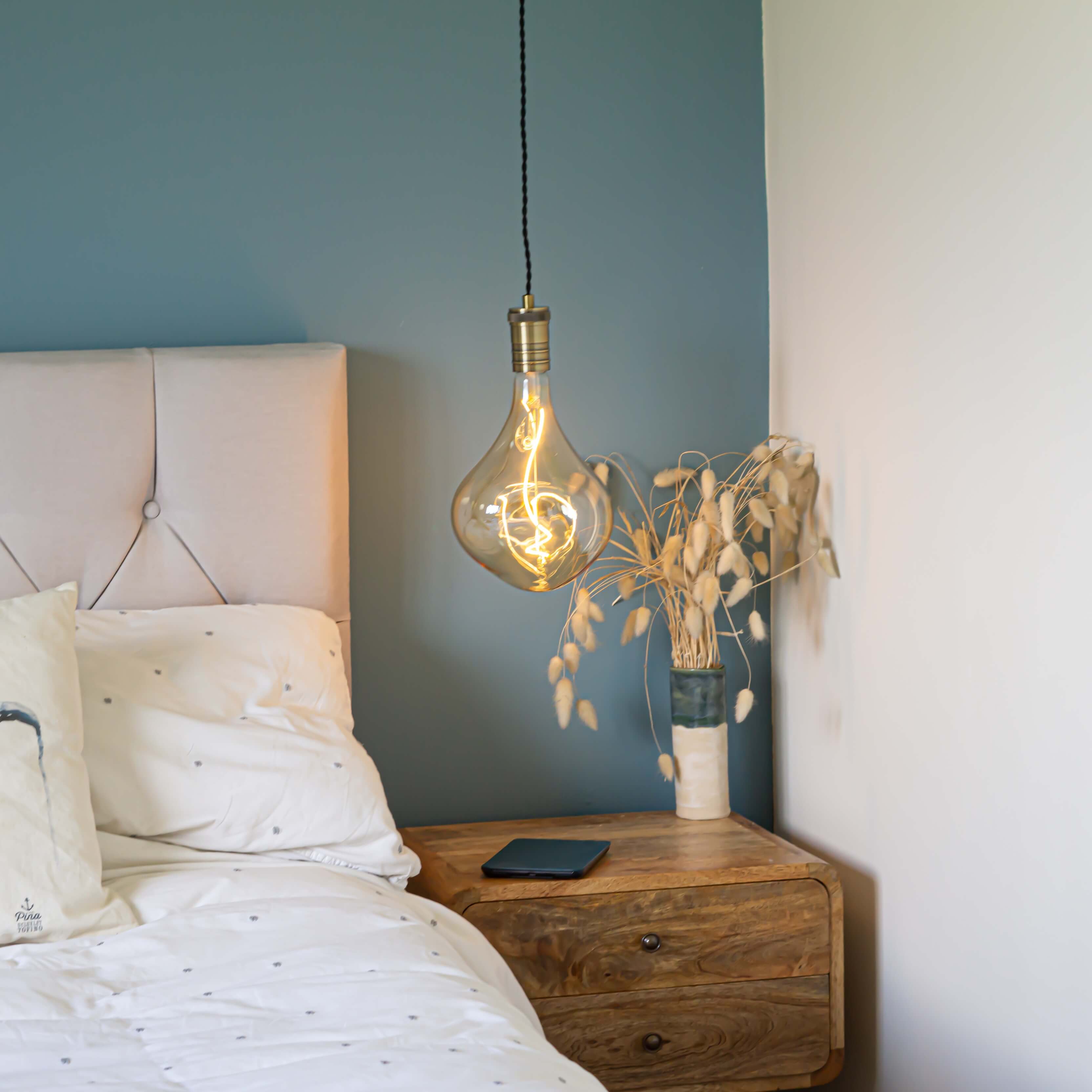 antique bronze pendant light and twisted cable with celeste bulb hanging above the bedside table in the bedroom