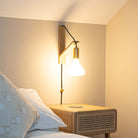 astrid plug in brass wall light with straight cable mounted by a bed