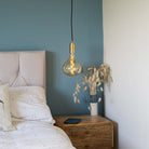 brass pendant light and straight cable with olivia bulb hanging above the bedside table