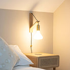 brass plug in brass wall light with twisted cable mounted by a bed
