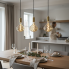 Dining table set with plates, glasses, and candles, featuring three hanging light bulbs.