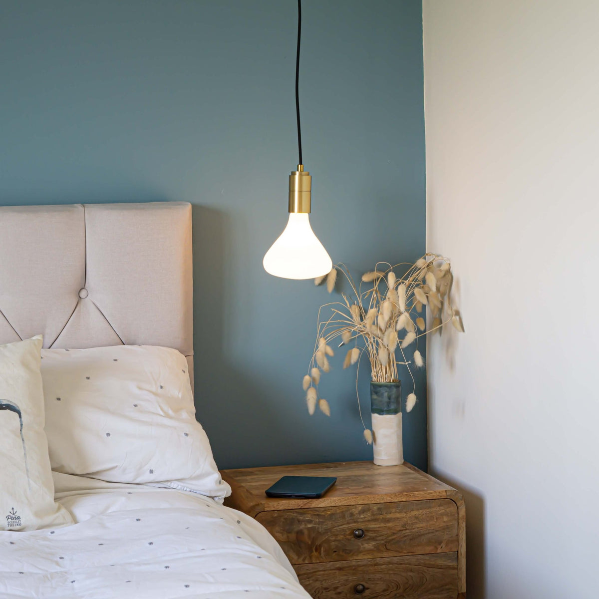 brass pendant light and straight cable with astrid bulb hanging above the bedside table 