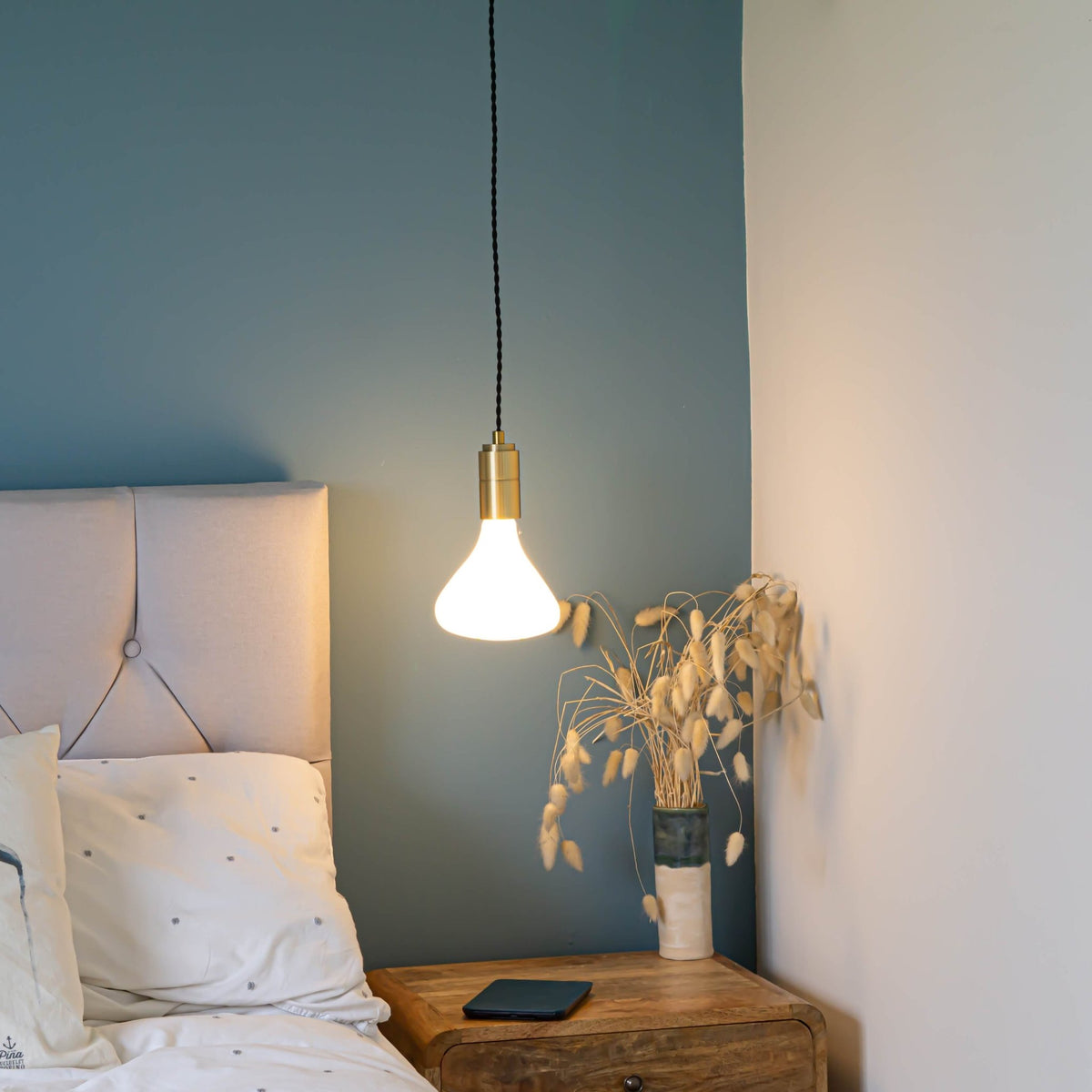 brass pendant light and twisted cable with astrid bulb hanging above the bedside table 