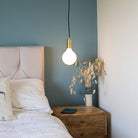 brass pendant light and straight cable with luna bulb hanging above the bedside table 
