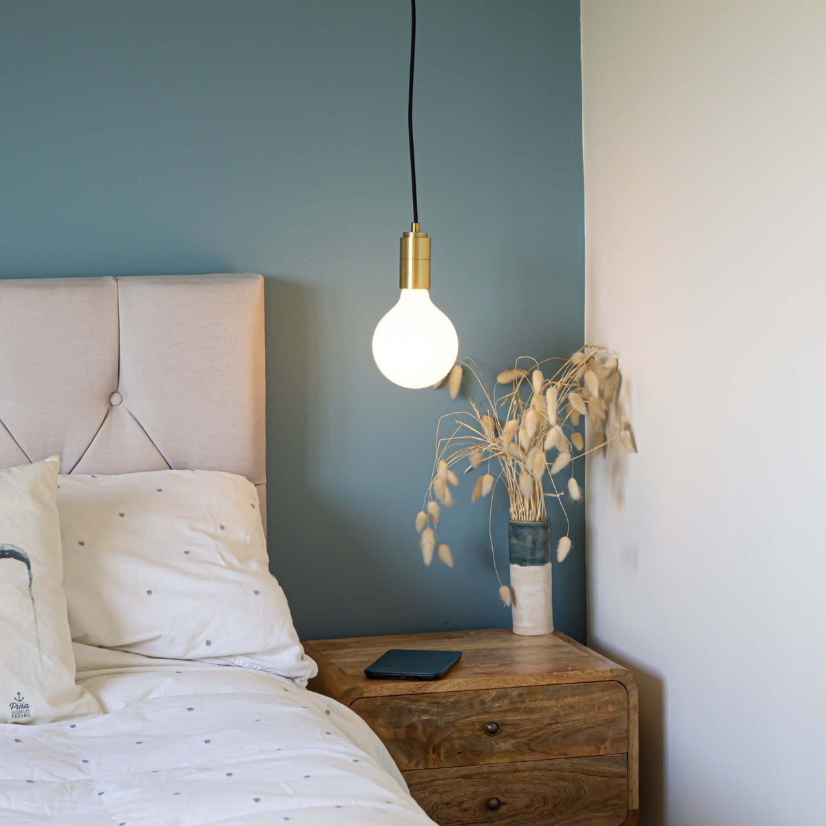 brass pendant light and straight cable with luna bulb hanging above the bedside table 