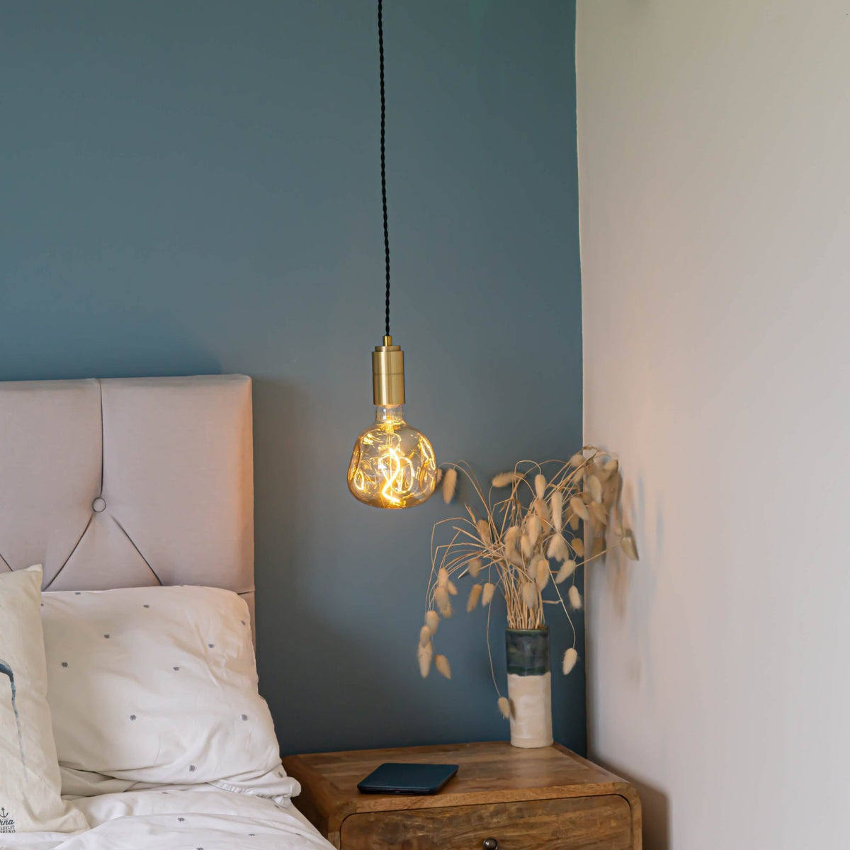 brass pendant light and twisted cable with isabella bulb hanging above the bedside table 