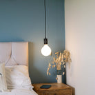 matte black pendant light with luna bulb hanging above the bedside table 