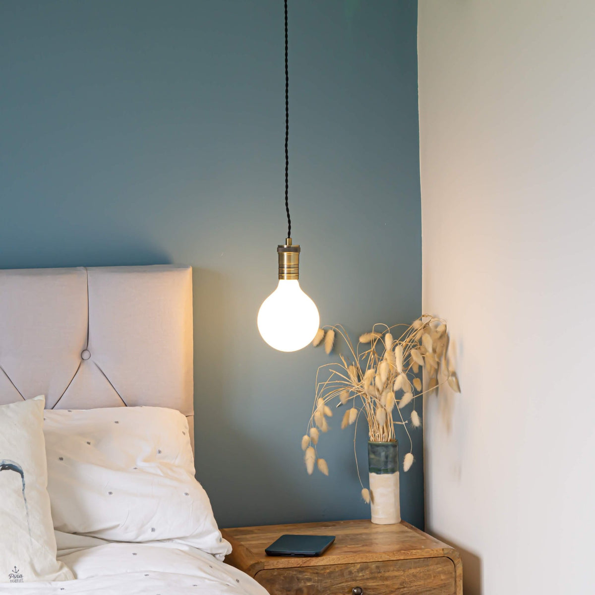 antique bronze pendant light and twisted cable with luna bulb hanging above the bedside table 