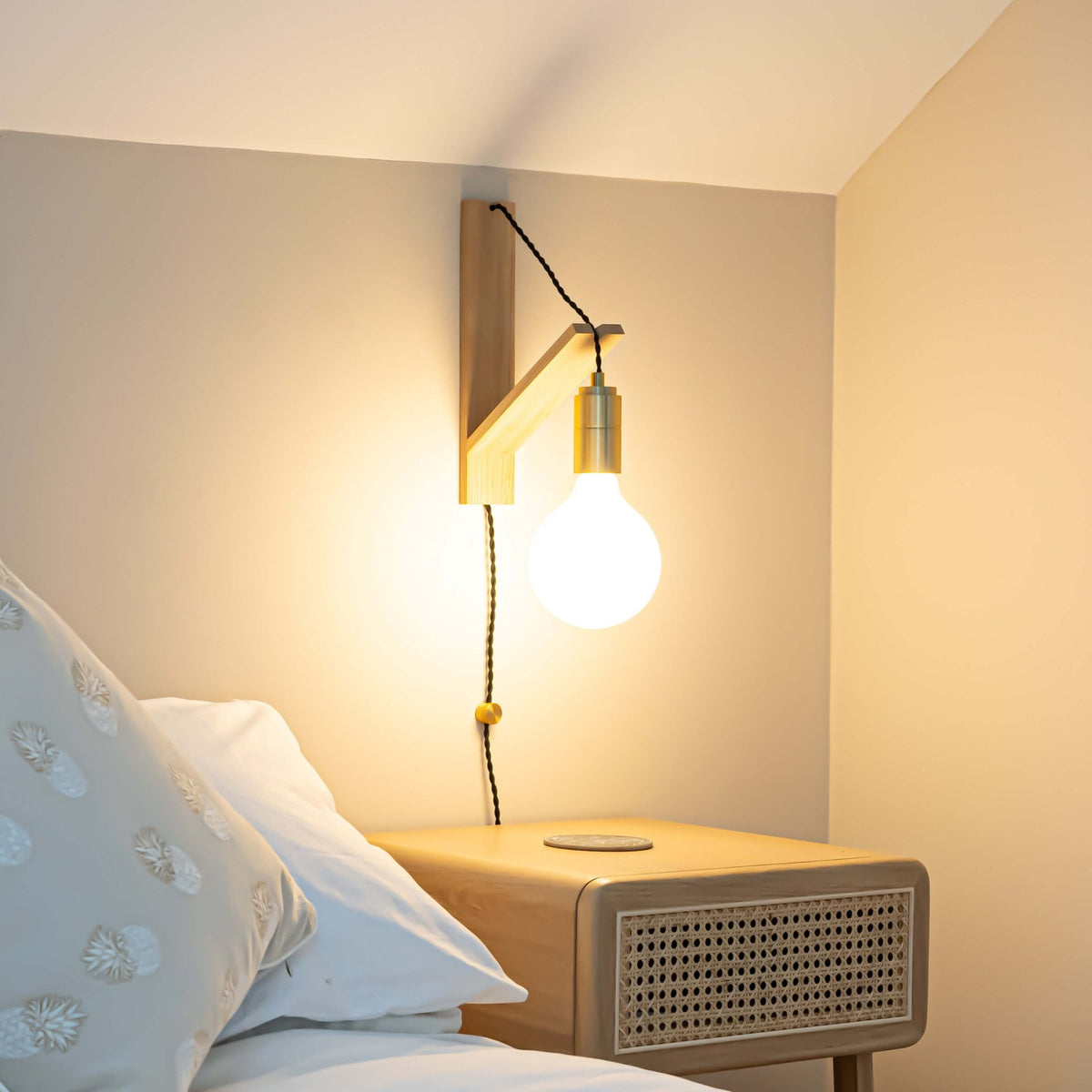 luna plug in brass wall light with twisted cable mounted by a bed