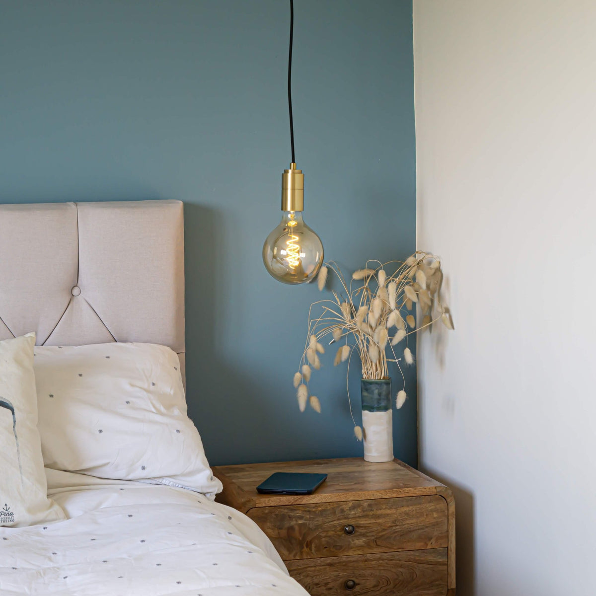 brass pendant light and straight cable with sophia bulb hanging above the bedside table 