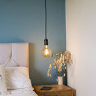 matte black pendant light with sophia bulb hanging above the bedside table 