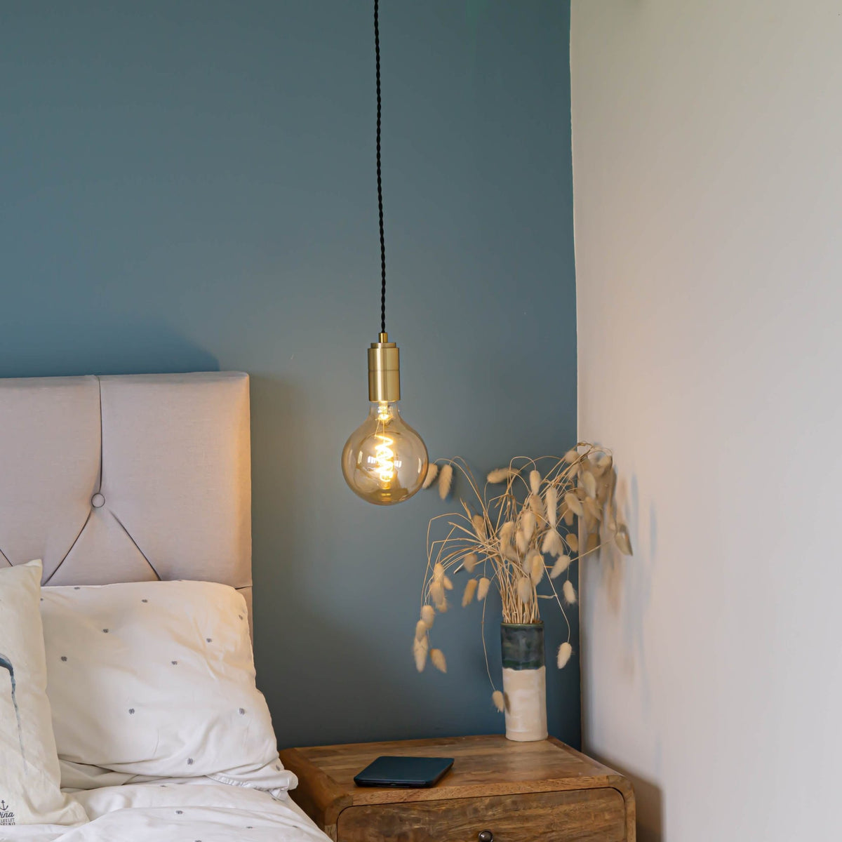 brass pendant light and twisted cable with sophia bulb hanging above the bedside table 